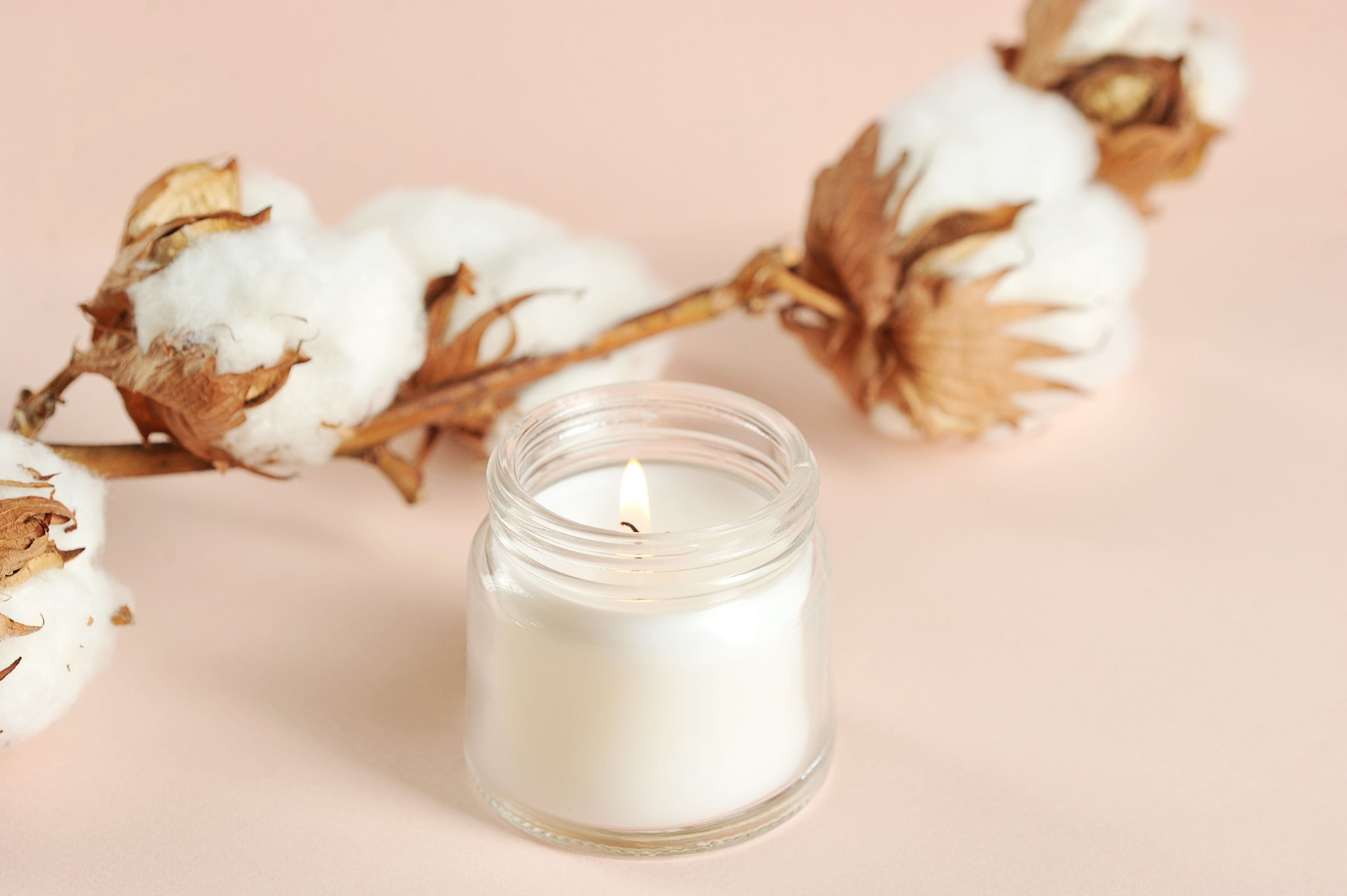 A cotton flower and a white candle in a glass jar.